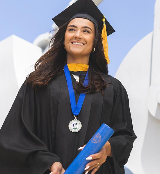 A UWF graduate wearing cap and gown and smiling